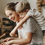A mom cooking with her son on her back in the kitchen