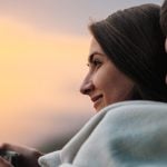 A couple cuddled under a blanket looking at the sunset outside