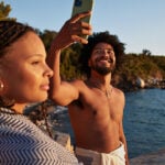 Man and woman on beach and man has mobile phone in hand as example of is sexting cheating