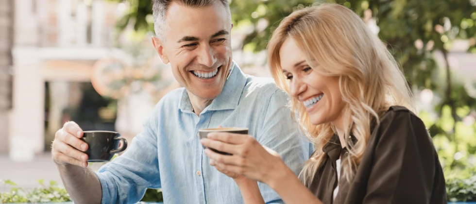 Dating couple sitting outside enjoying a cup of coffee while laughing and having fun.
