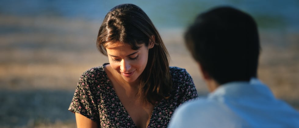 a woman sitting in front of a man, looking shyly at the ground as a symbol of introvert dating