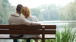 A couple is sitting on a bench in front of a lake. (Generated with AI)