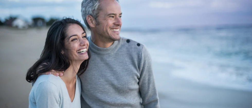 A couple standing side by side at the beach looking at the waves.