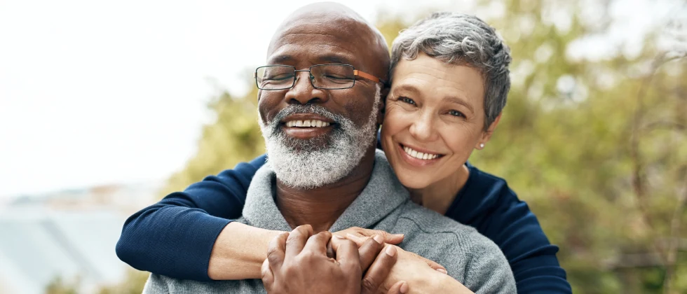 A woman hugging a man from behind, both are smiling.